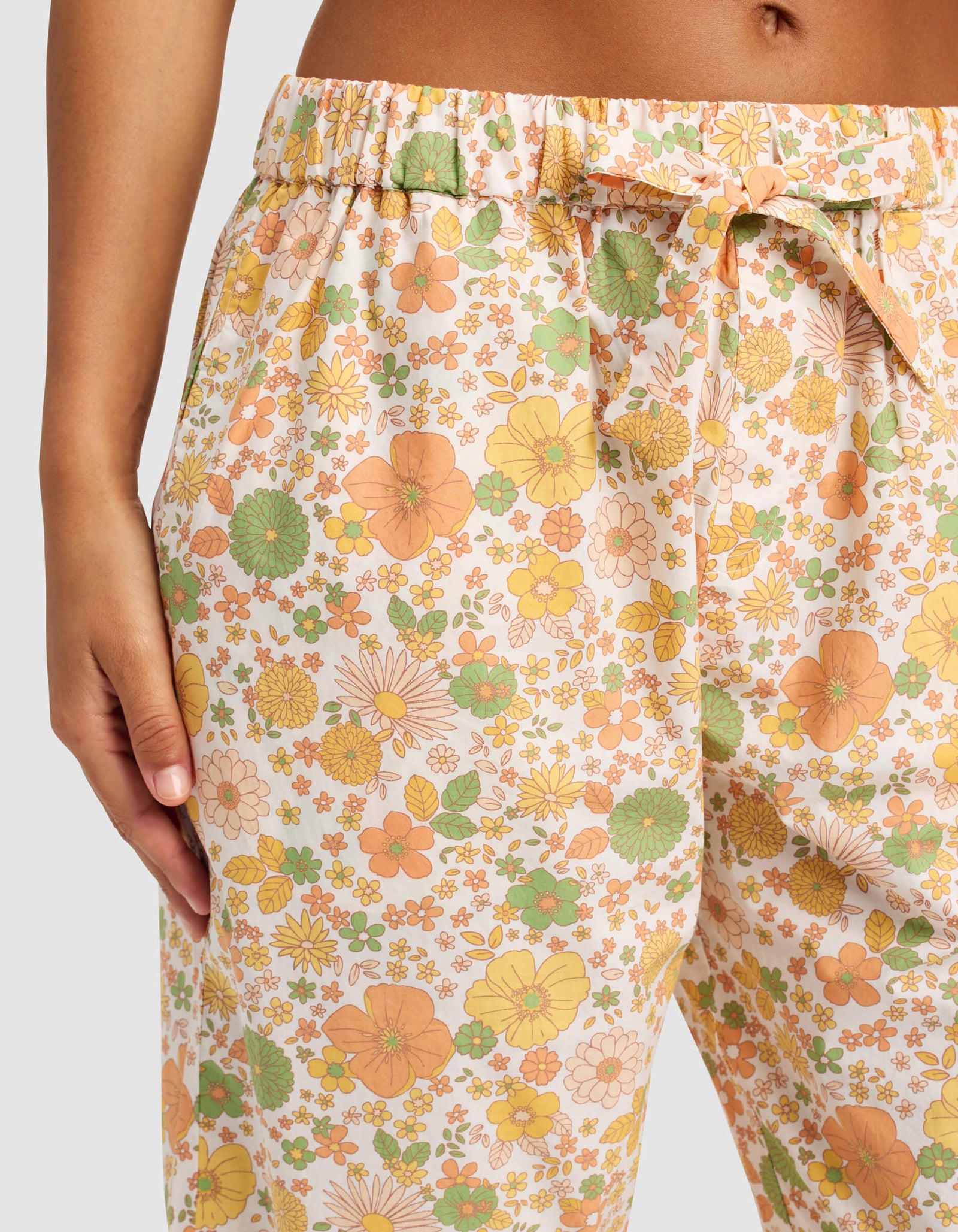 A person wearing Cozy Earth’s Women's Sutton Short Sleeve & Pant Pajama Set—high-waisted, loose-fitting pants with an orange, yellow, and green floral pattern and a drawstring waistband—rests their hand in one pocket.