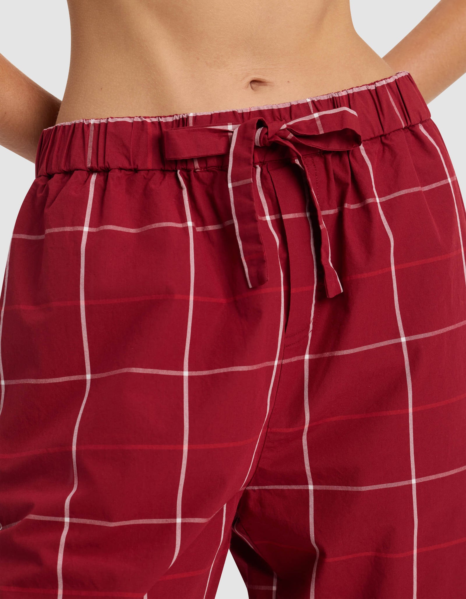 Close-up of a person wearing Cozy Earth's Women's Sutton Pajama Pant, featuring a red and white plaid pattern with a drawstring waist.