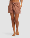 A person stands barefoot with hands in the pockets of light brown Women's Sutton Pajama Shorts by Cozy Earth, shown mid-thigh length against a plain light background.|Color:Saddle