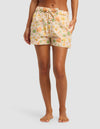 A person stands barefoot wearing Cozy Earth's Women's Sutton Pajama Short, featuring an orange, green, and white floral print with a drawstring waist and side pockets. Only the lower body is visible against a plain background.|Color:Wildflower