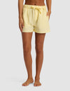 A person stands barefoot, hands in pockets, wearing Cozy Earth's Women's Sutton Pajama Short in light yellow with a waistband tie, against a plain light background.|Color:Meringue