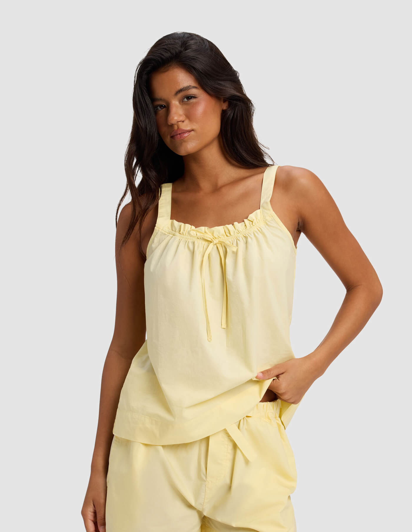A woman with long dark hair wears the Cozy Earth Women's Sutton Tank & Cropped Pant Pajama Set in light yellow, posing against a plain light gray background.