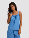 A woman with long dark hair wears the Cozy Earth Women's Sutton Pajama Tank in light blue, paired with matching blue pants, standing against a plain light gray background.|Color:Sailor
