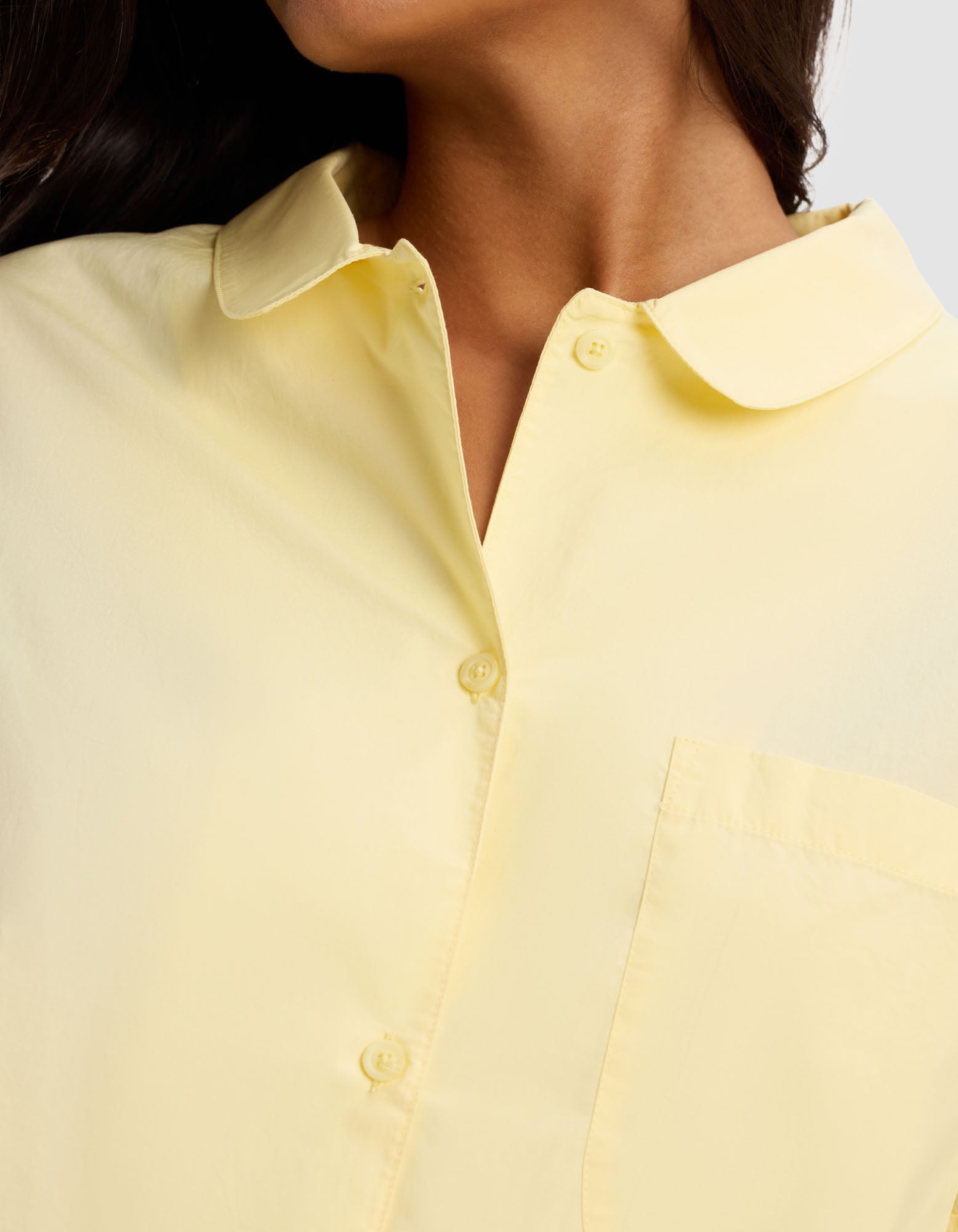 Close-up of a person wearing the Cozy Earth Women's Sutton Short Sleeve Pajama Top in pale yellow, featuring a collar and front pocket; focus is on the upper torso and neck with head partially visible, turned to the side.