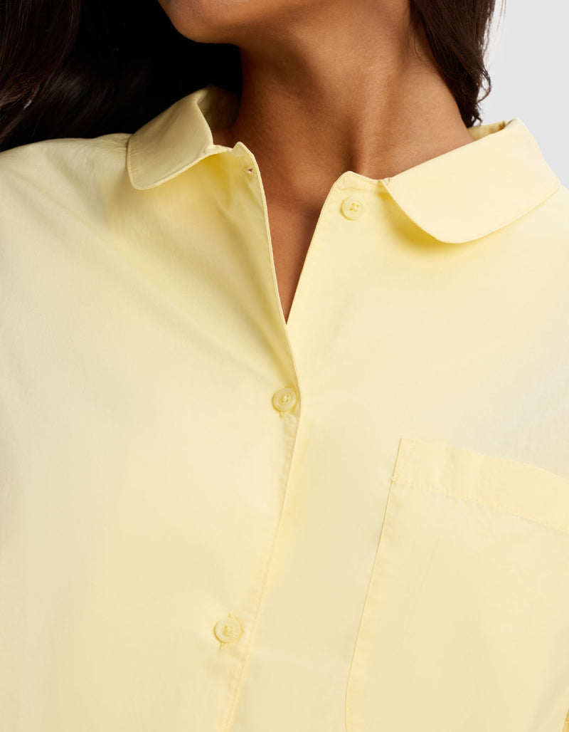 Close-up of a person wearing the Cozy Earth Women's Sutton Short Sleeve Pajama Top in pale yellow, featuring a collar and front pocket; focus is on the upper torso and neck with head partially visible, turned to the side.
