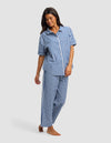 A woman models the Cozy Earth Women's Sutton Short Sleeve & Pant Pajama Set, featuring a blue and white checkered design, standing barefoot against a plain light gray background.|Color:Pacific Gingham