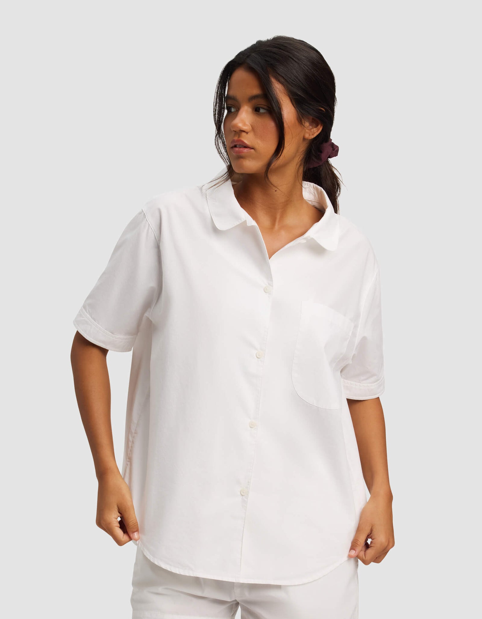 A woman stands against a plain light gray background wearing the Cozy Earth Women's Sutton Short Sleeve Pajama Top in white, paired with matching white shorts.