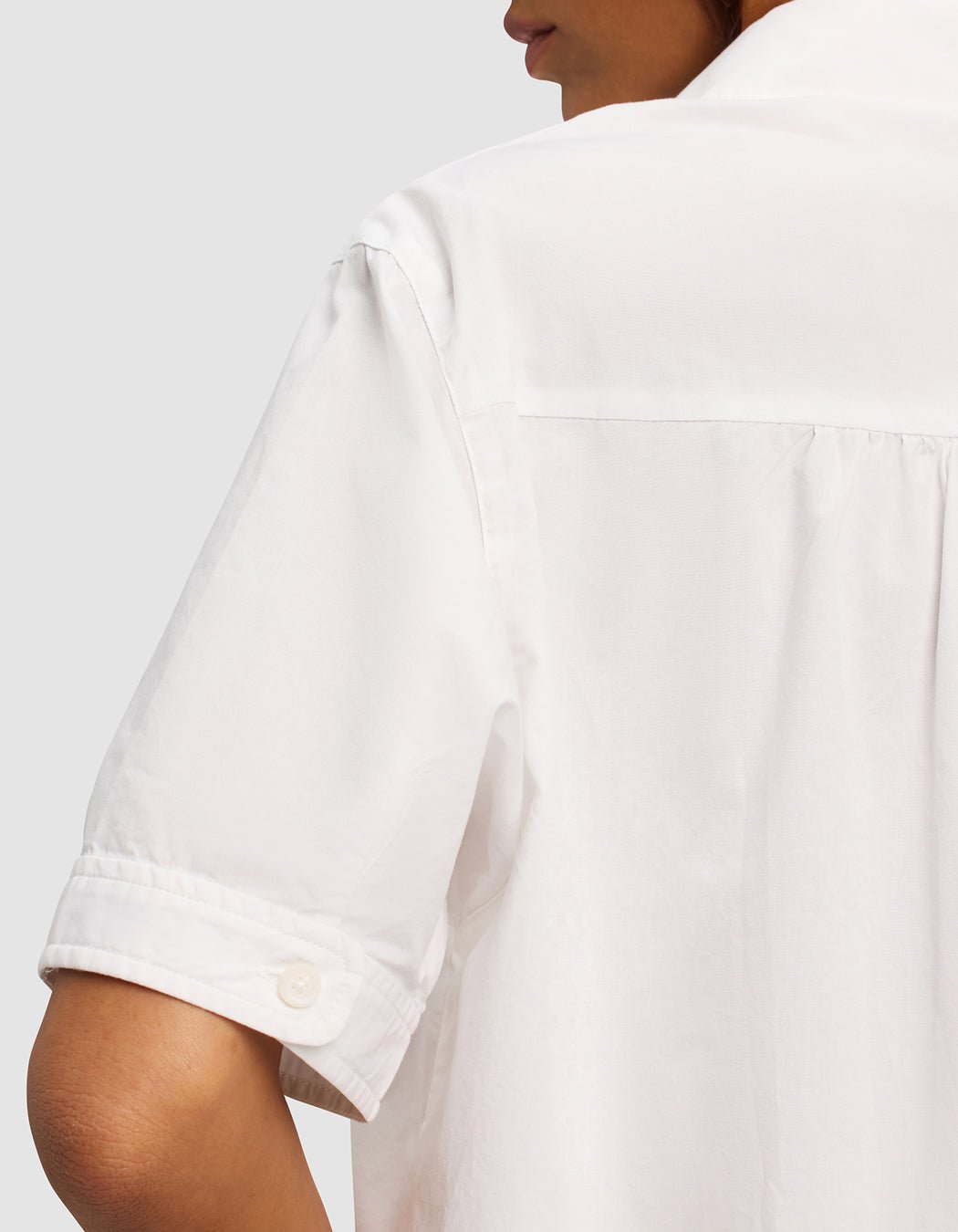 Close-up of a woman wearing the Cozy Earth Women's Sutton Short Sleeve Pajama Top, shown from the back and side. Focus on the sleeve, cuff button, and back shoulder detail. Background is plain light gray.