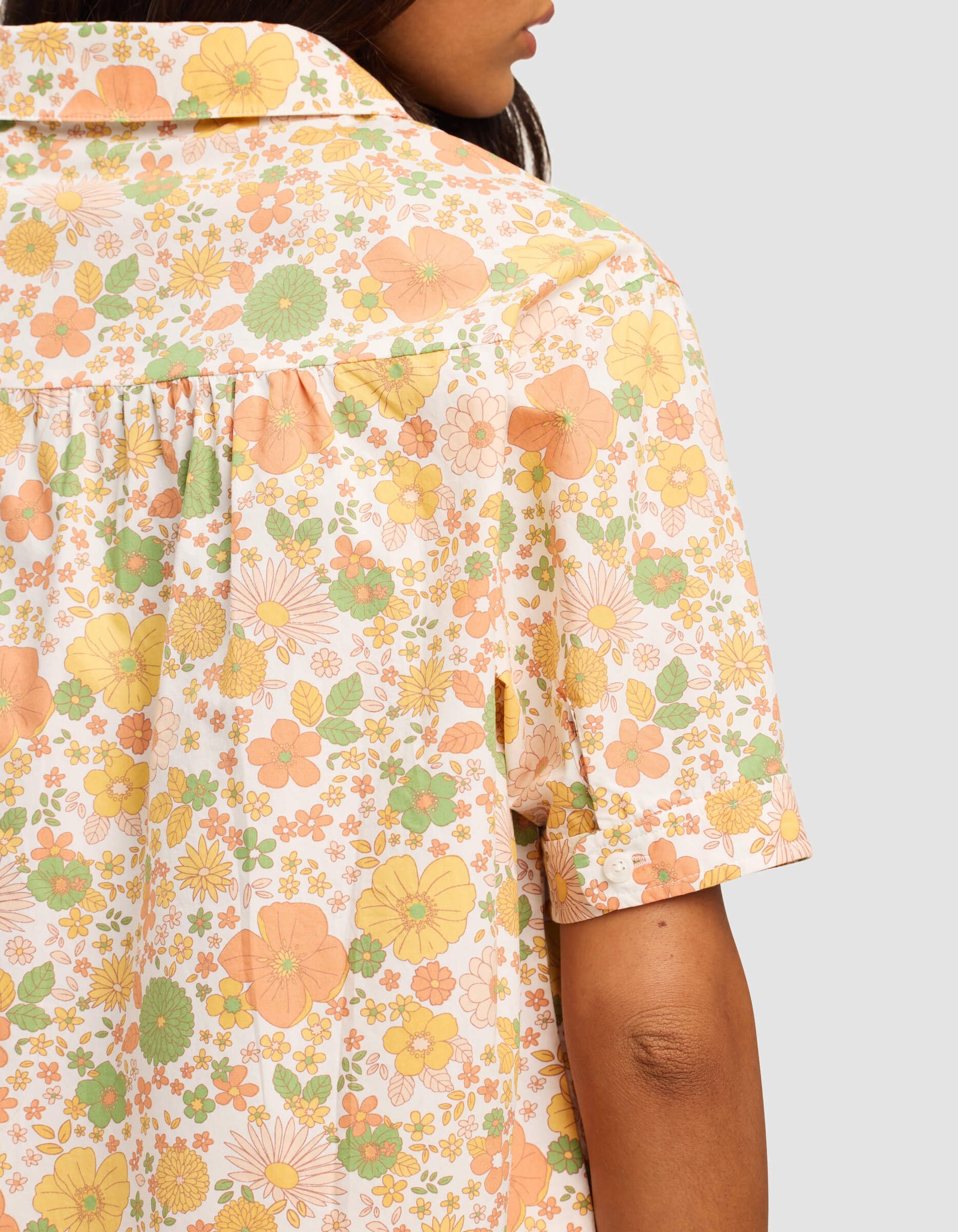 A woman is seen from the back in the Cozy Earth Women's Sutton Short Sleeve Pajama Top, featuring a vibrant yellow, orange, and green floral pattern against a plain background.