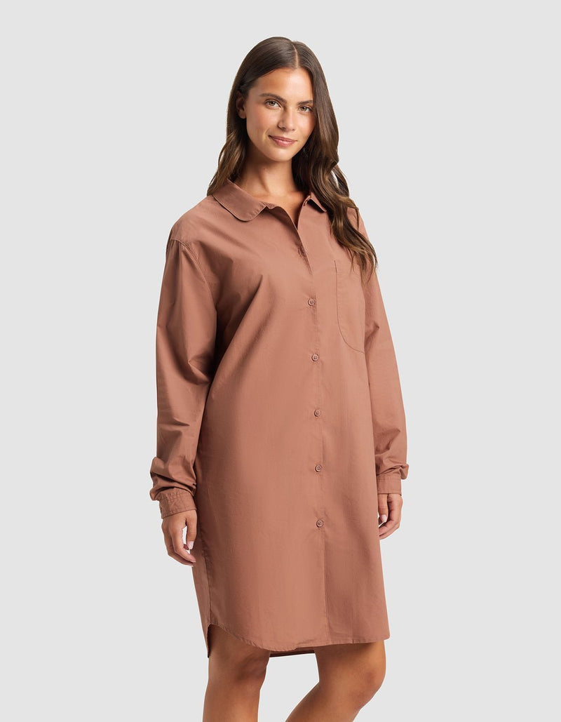 A woman smiles slightly against a plain light gray background, wearing the Cozy Earth Women's Sutton Sleep Dress—a loose-fitting, long-sleeve, button-down shirt dress in brownish-pink with a collared neckline and chest pocket.