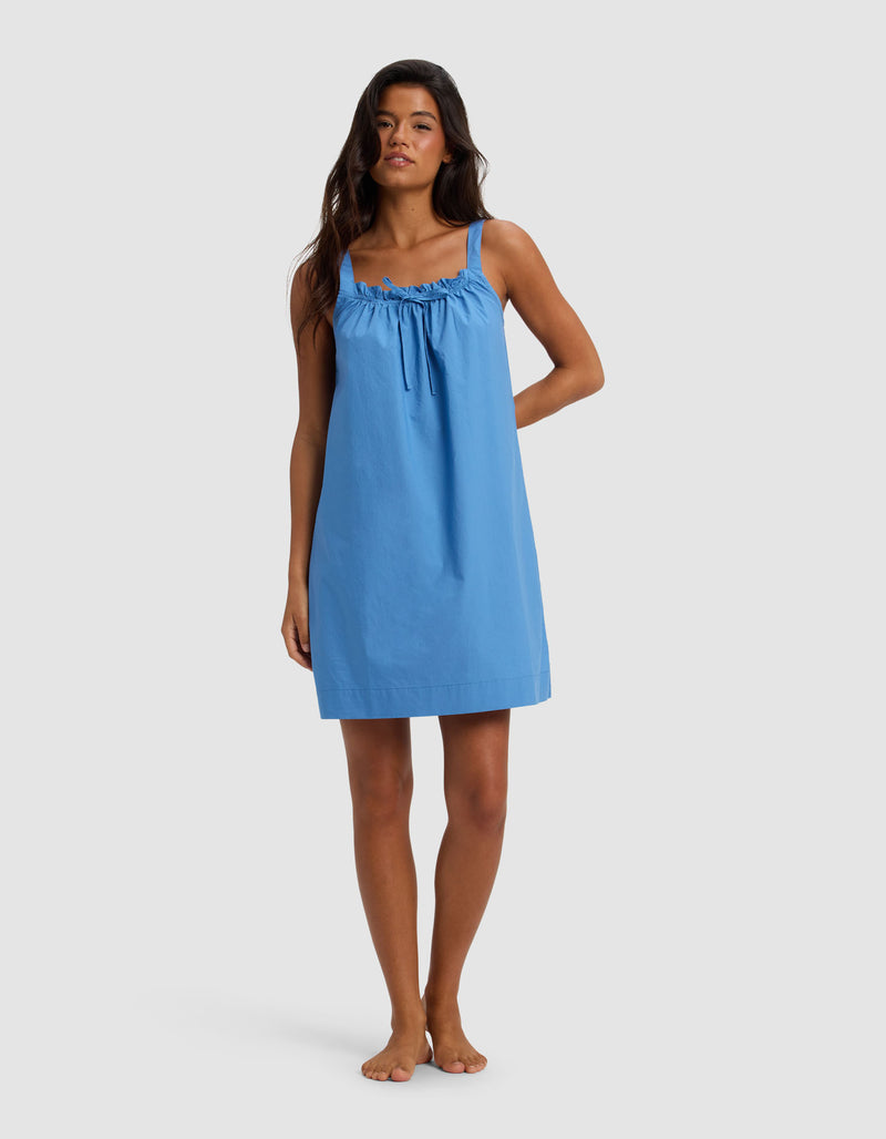 A woman stands barefoot against a plain background, wearing the Cozy Earth Women's Sutton Tank Sleep Dress in Sailor—a loose-fitting, sleeveless style with gathered neckline detail and thin shoulder straps.