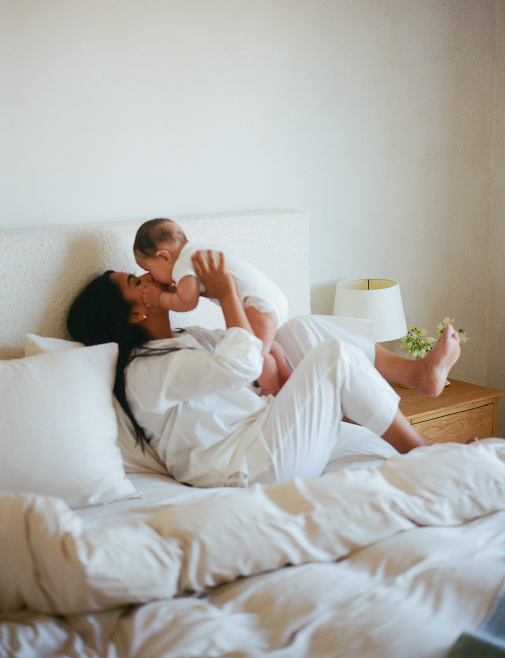 Woman and child in bed, surrounded by white bedding and pillows.