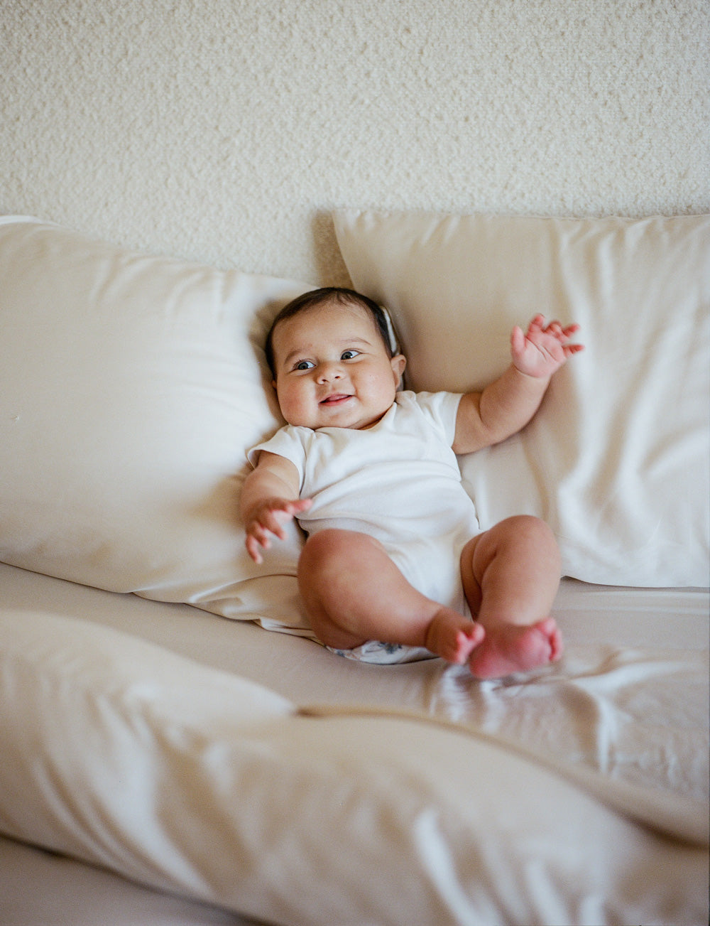 Baby in a white onesie sitting on a bed