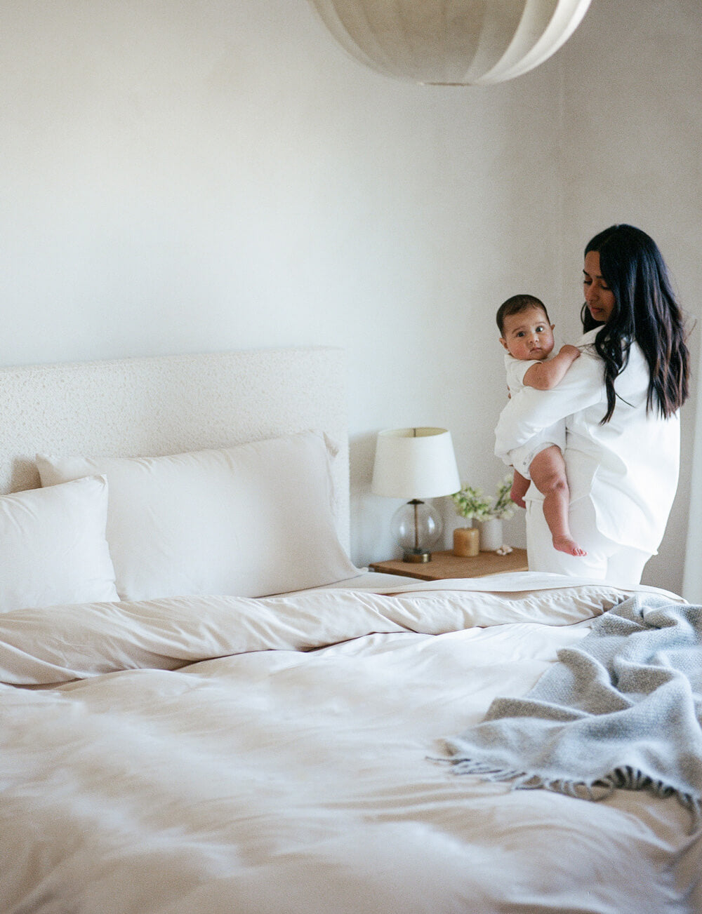 Woman holding a baby in a bedroom with white bedding and decor