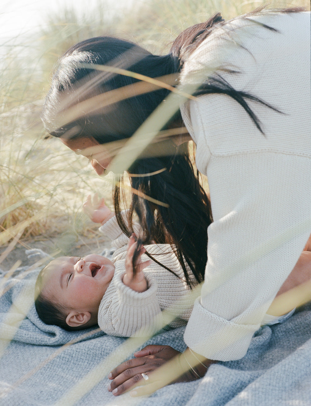 Woman lies over a baby on a blanket in a grassy field