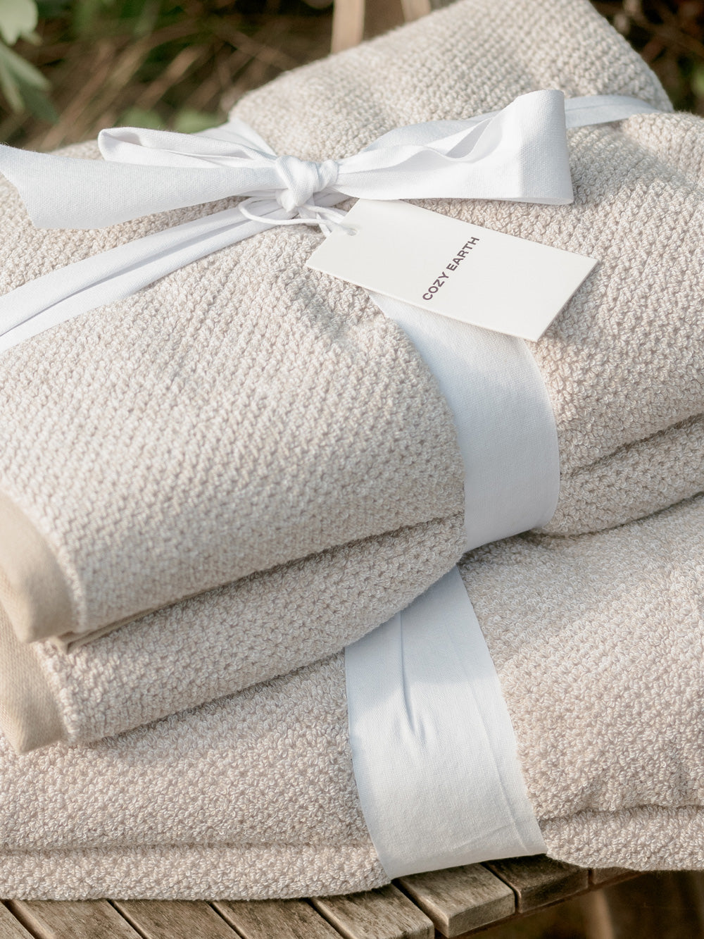 Stack of beige towels with white ribbons and a tag on a wooden surface.