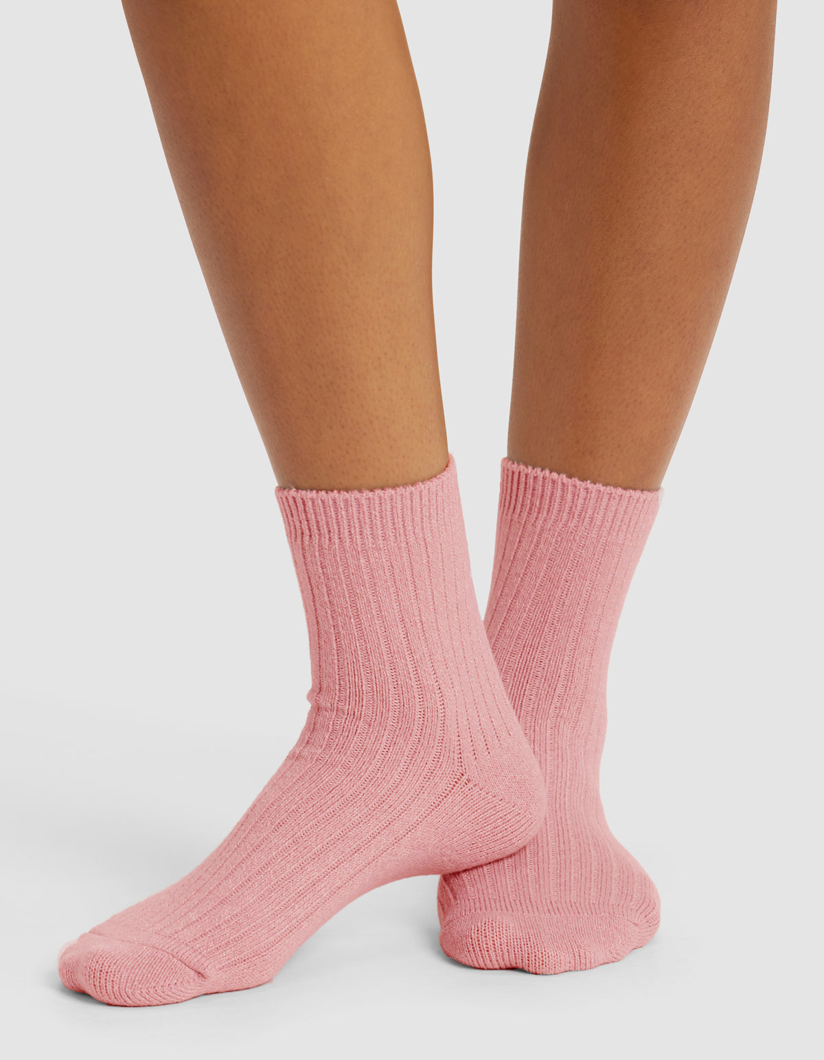 Close-up of a person wearing Cozy Earth's The Plush Modern Crew Sock in light pink, standing on a white surface with legs crossed at the ankles.|Color:Tulip