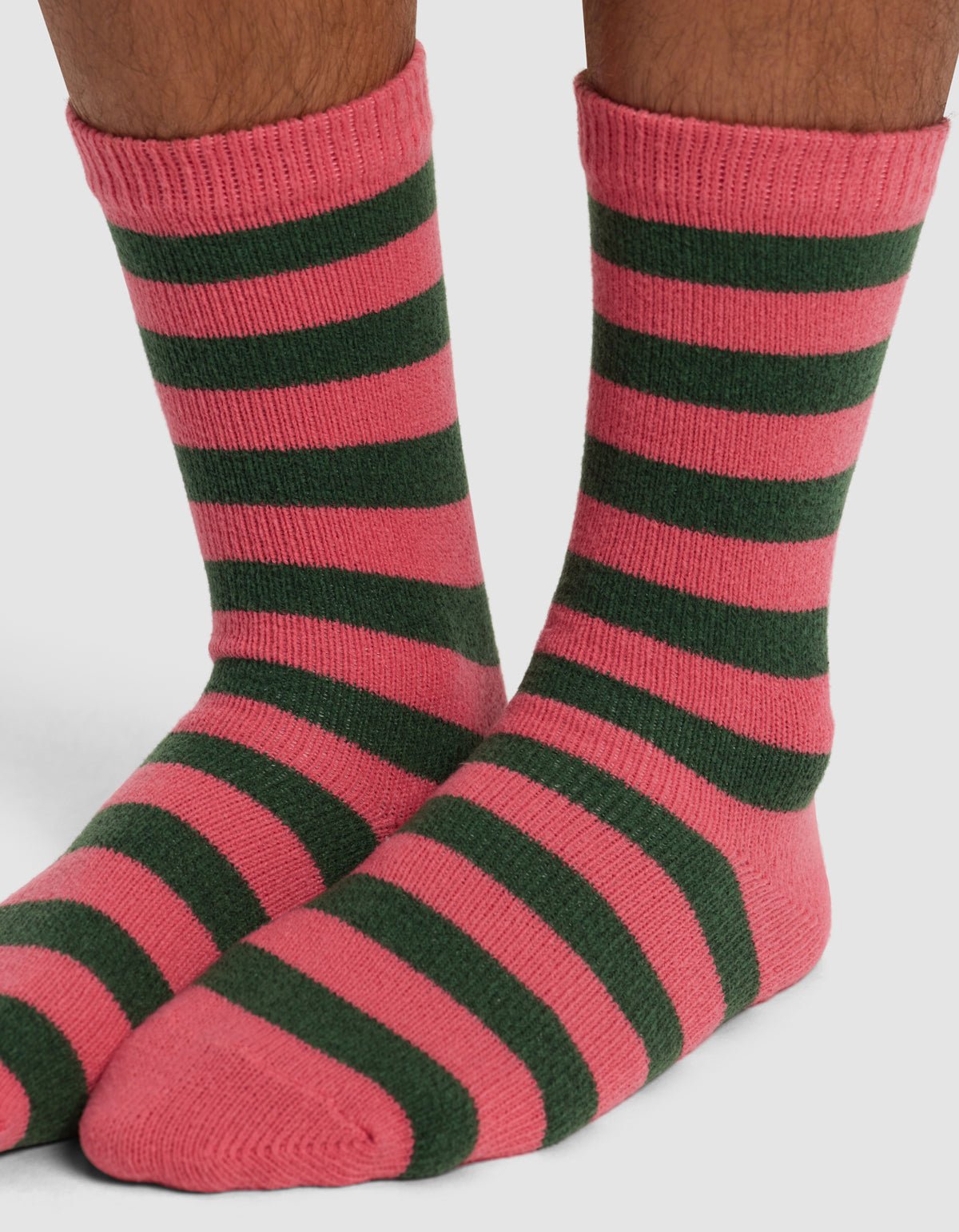 A pair of feet wear Cozy Earth's Striped Plush Lounge Socks, featuring horizontal pink and dark green stripes, against a plain white background.|Color:Hibiscus Stripe