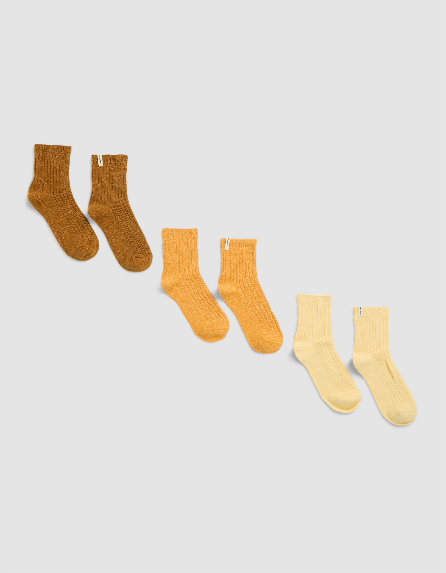 Three pairs of Plush Lounge Quarter Socks by Cozy Earth are arranged in a row on a light background, each in a different color: brown, orange, and light yellow.|Color:Nubuck/Amber/Daisy