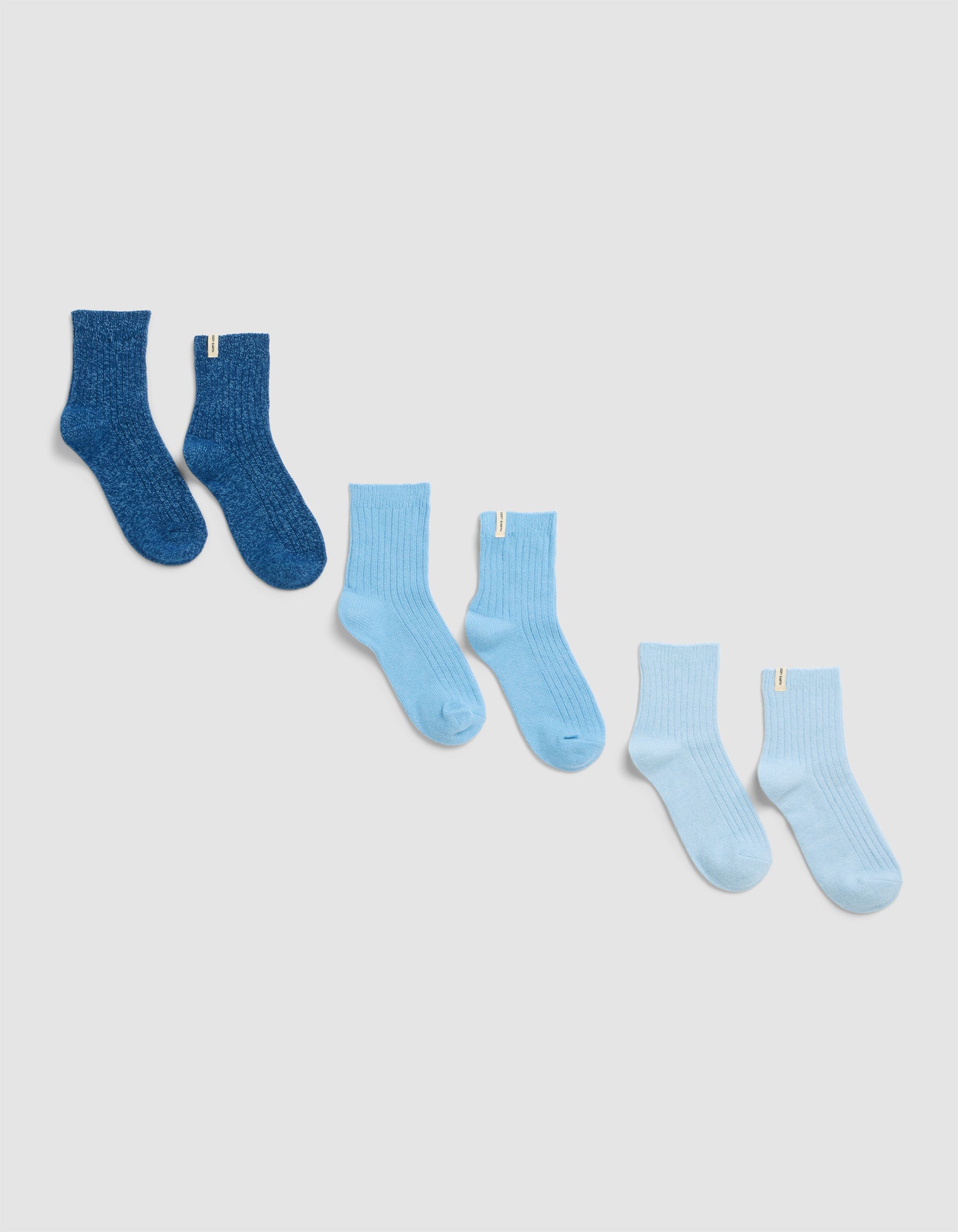 Four pairs of Cozy Earth’s Plush Lounge Quarter Socks, in gradient blue shades from dark to very light, are arranged diagonally on a plain light background.