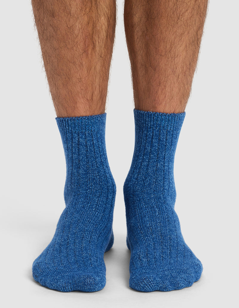 A pair of feet wearing Cozy Earth's Plush Lounge Quarter Socks from the 3-Pack, in blue. The socks are thick and ribbed, and the wearer stands on a white surface with their lower legs showing.