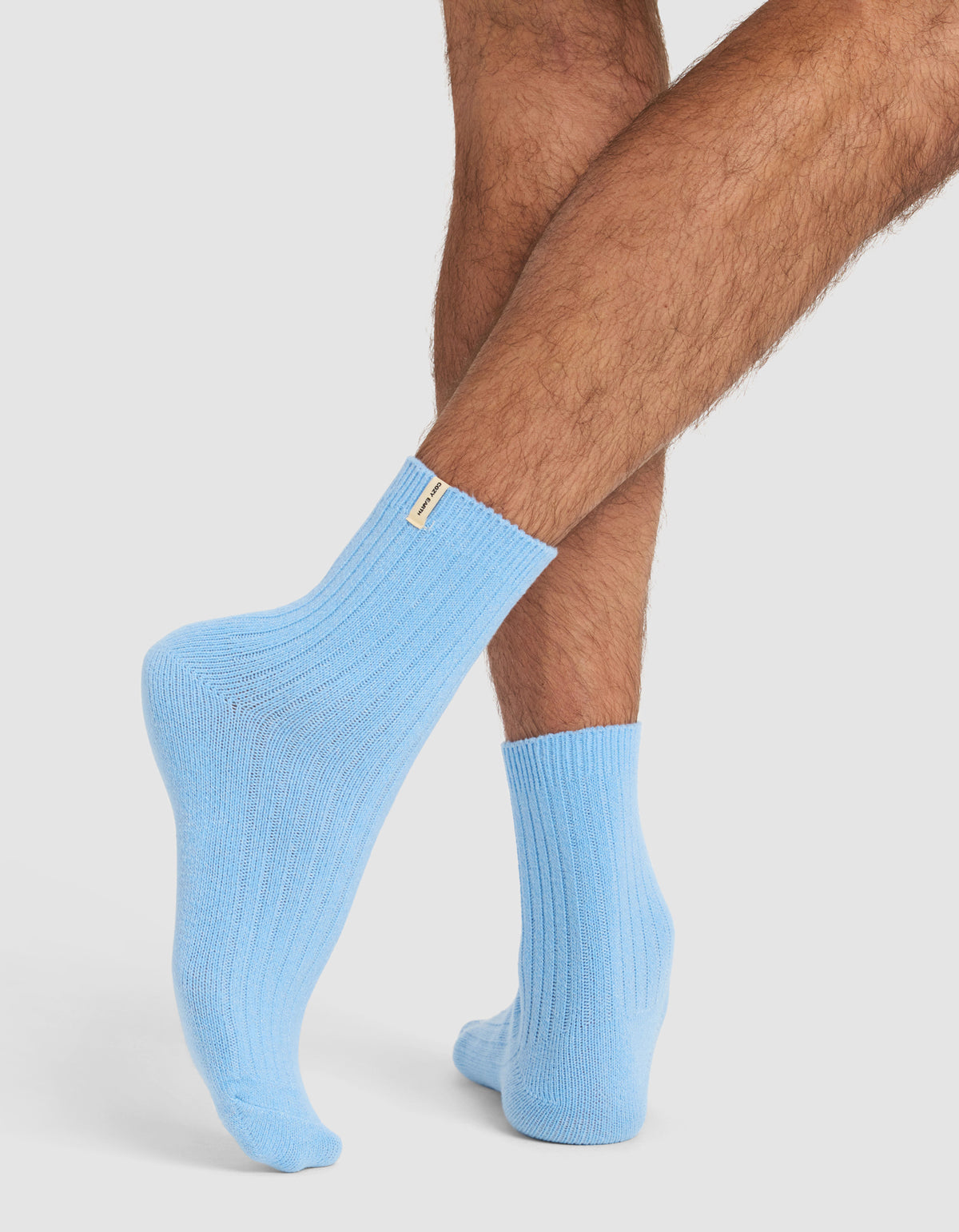 A person with crossed legs wearing Cozy Earth’s The Plush Modern Crew Sock 3-Pack in light blue, standing against a plain light background.