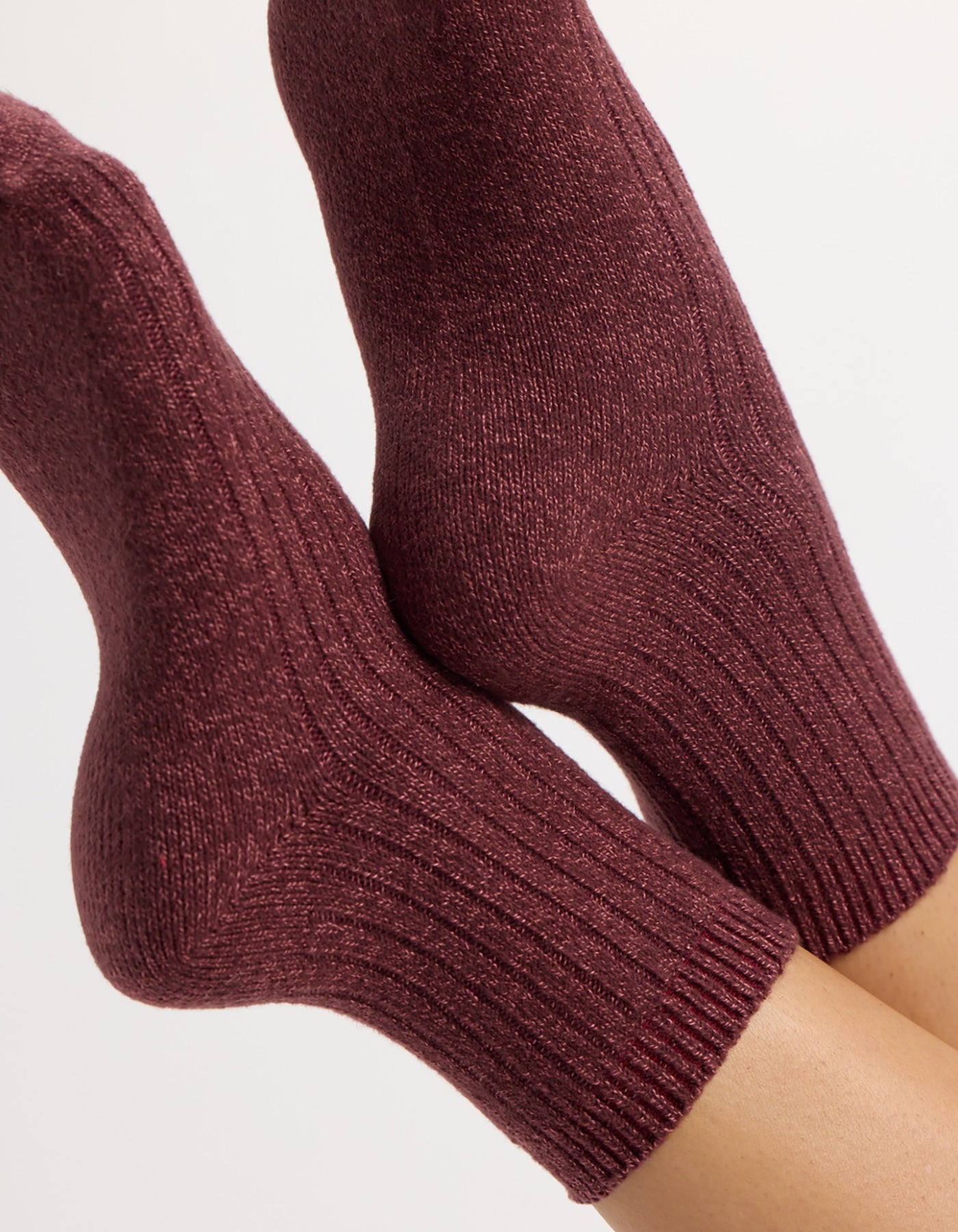 A pair of feet wear Cozy Earth's The Plush Modern Crew Sock (3-Pack) in burgundy, featuring a cozy ribbed knit and textured pattern, shown against a plain light background.