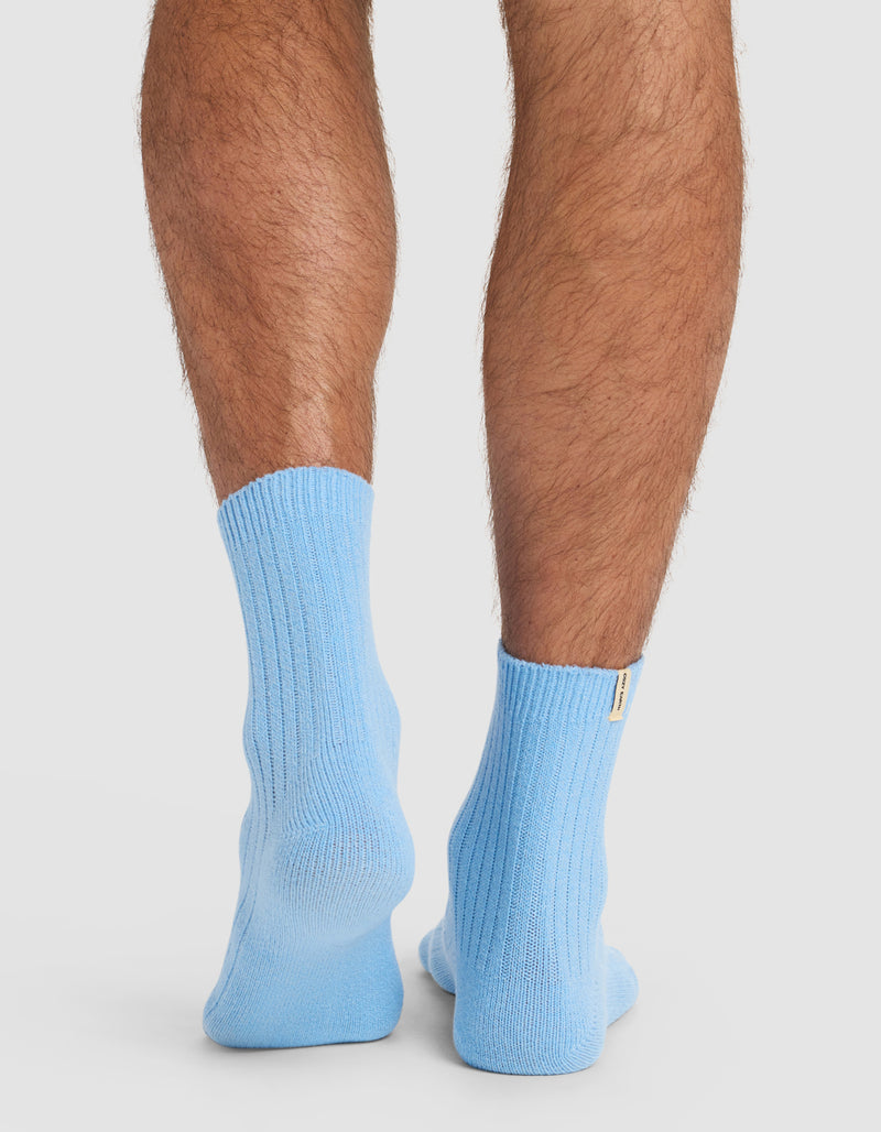 A close-up of a person's lower legs and feet from behind, wearing Cozy Earth’s Plush Lounge Quarter Sock in light blue, set against a plain white background.