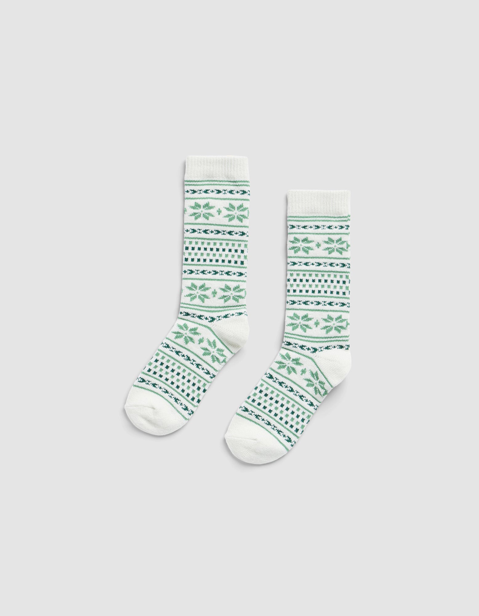 The Snowflake Plush Lounge Sock by Cozy Earth, a pair of white crew socks with green and blue geometric and floral patterns, displayed flat on a plain light gray background.