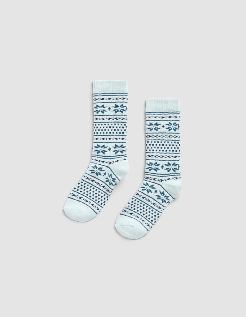 The Cozy Earth Snowflake Plush Lounge Sock features light blue fabric with dark blue geometric and snowflake stripes, shown on a plain light gray background.