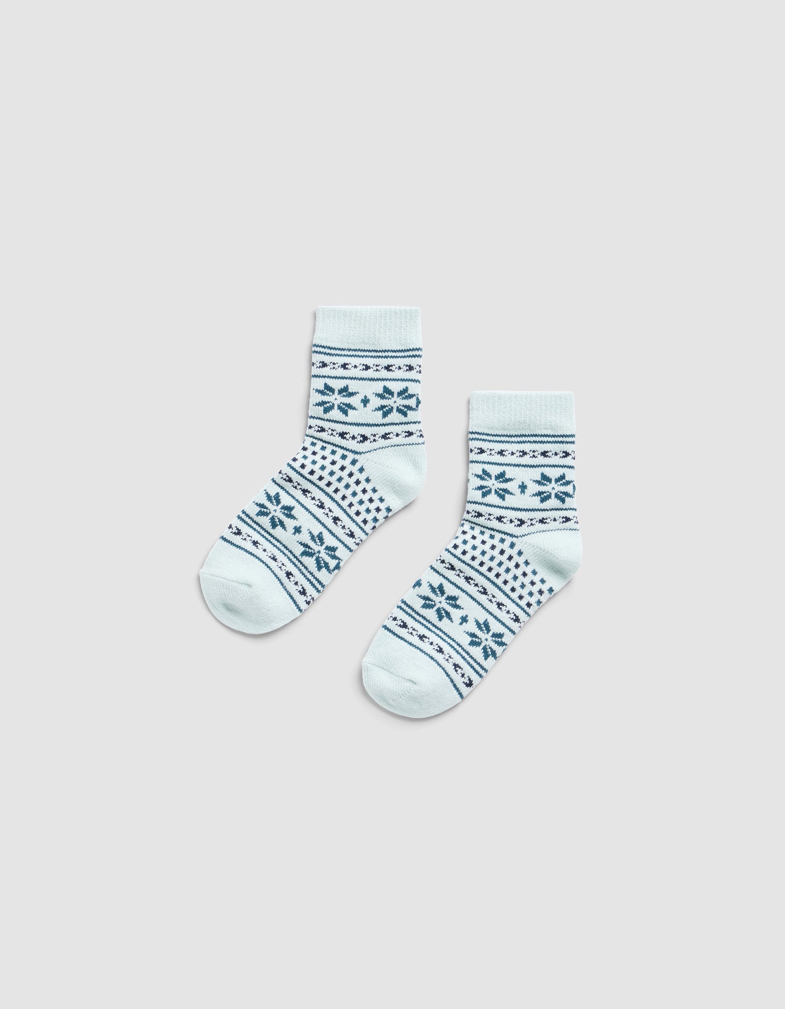 The Snowflake Plush Modern Crew Sock by Cozy Earth features light blue fabric with dark blue geometric and floral patterns, displayed flat on a light gray background.