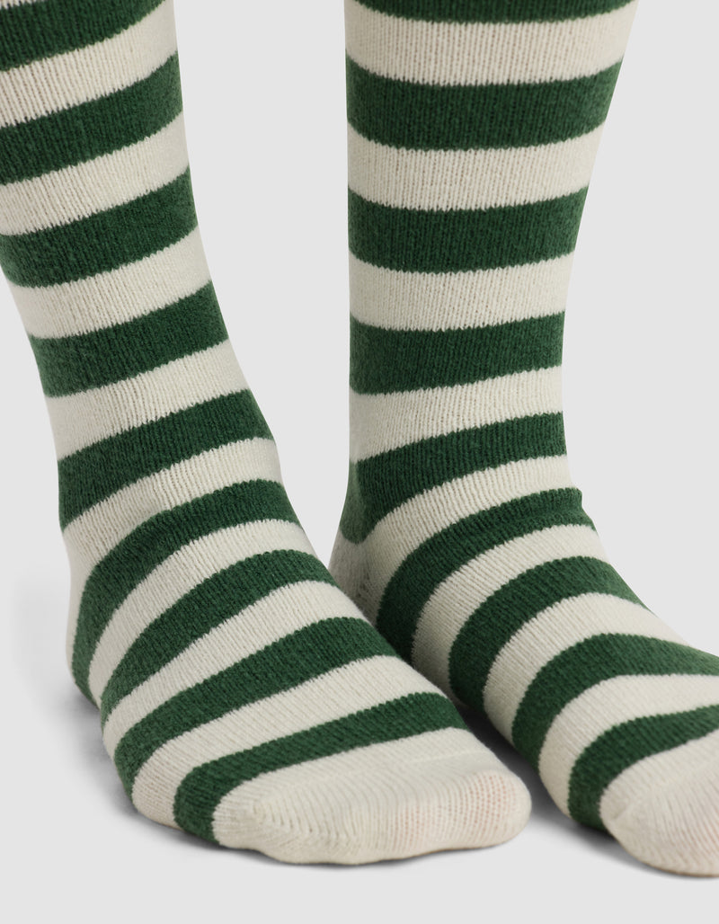 Close-up of feet wearing Cozy Earth's The Striped Plush Lounge Sock, featuring thick, horizontal dark green stripes on white, standing on a white background.
