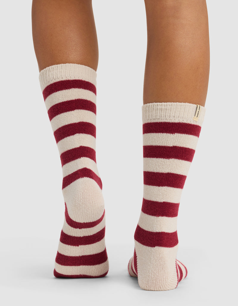 A person stands with their back to the camera, wearing Cozy Earth's The Striped Plush Lounge Sock in cream with bold red stripes, against a plain white background.