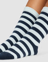 A close-up of two feet wearing Cozy Earth's Striped Plush Lounge Socks, featuring alternating thick black and white stripes, against a plain light background.|Color:Mist Stripe
