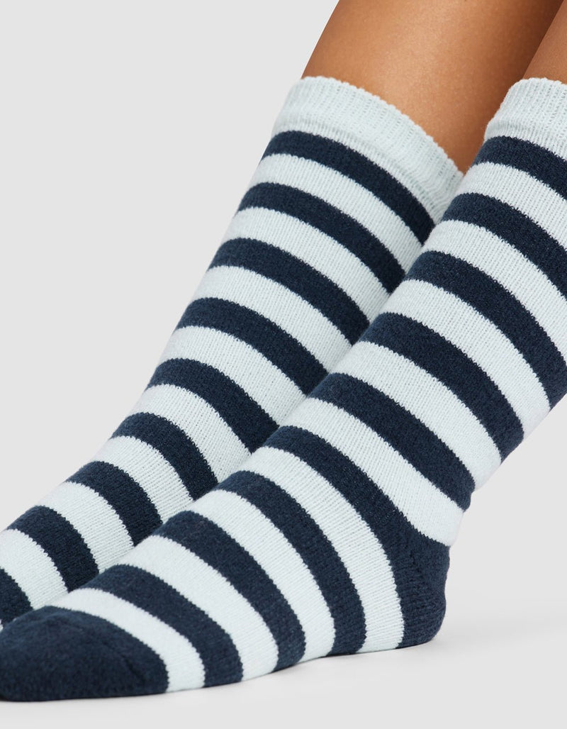 A close-up of two feet wearing Cozy Earth's Striped Plush Lounge Socks, featuring alternating thick black and white stripes, against a plain light background.