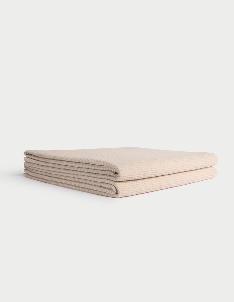 A neatly folded, light beige Cozy Earth Waffle Bath Towel lies on a white background.