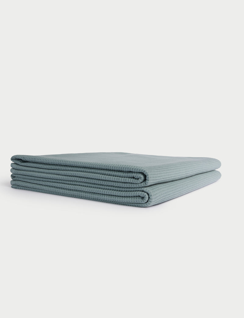 A neatly folded, light blue Cozy Earth Waffle Bath Towel is displayed on a white background.