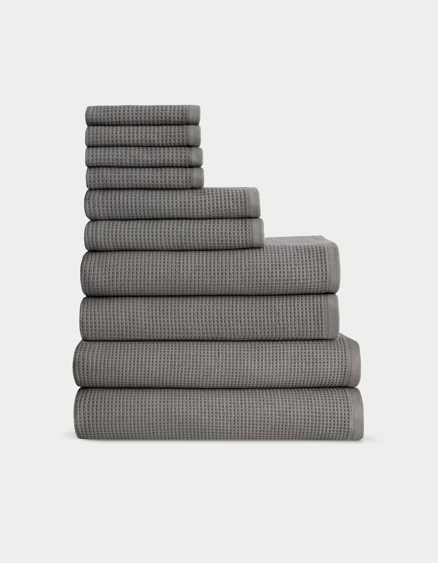 The Complete Waffle Bath Bundle by Cozy Earth features a neatly stacked set of dark gray waffle-textured towels, arranged from largest to smallest, against a plain white background.