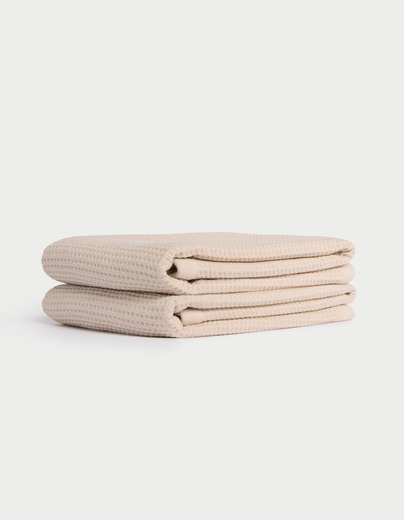 Two neatly folded beige Cozy Earth Waffle Hand Towels stacked atop each other against a plain white background.