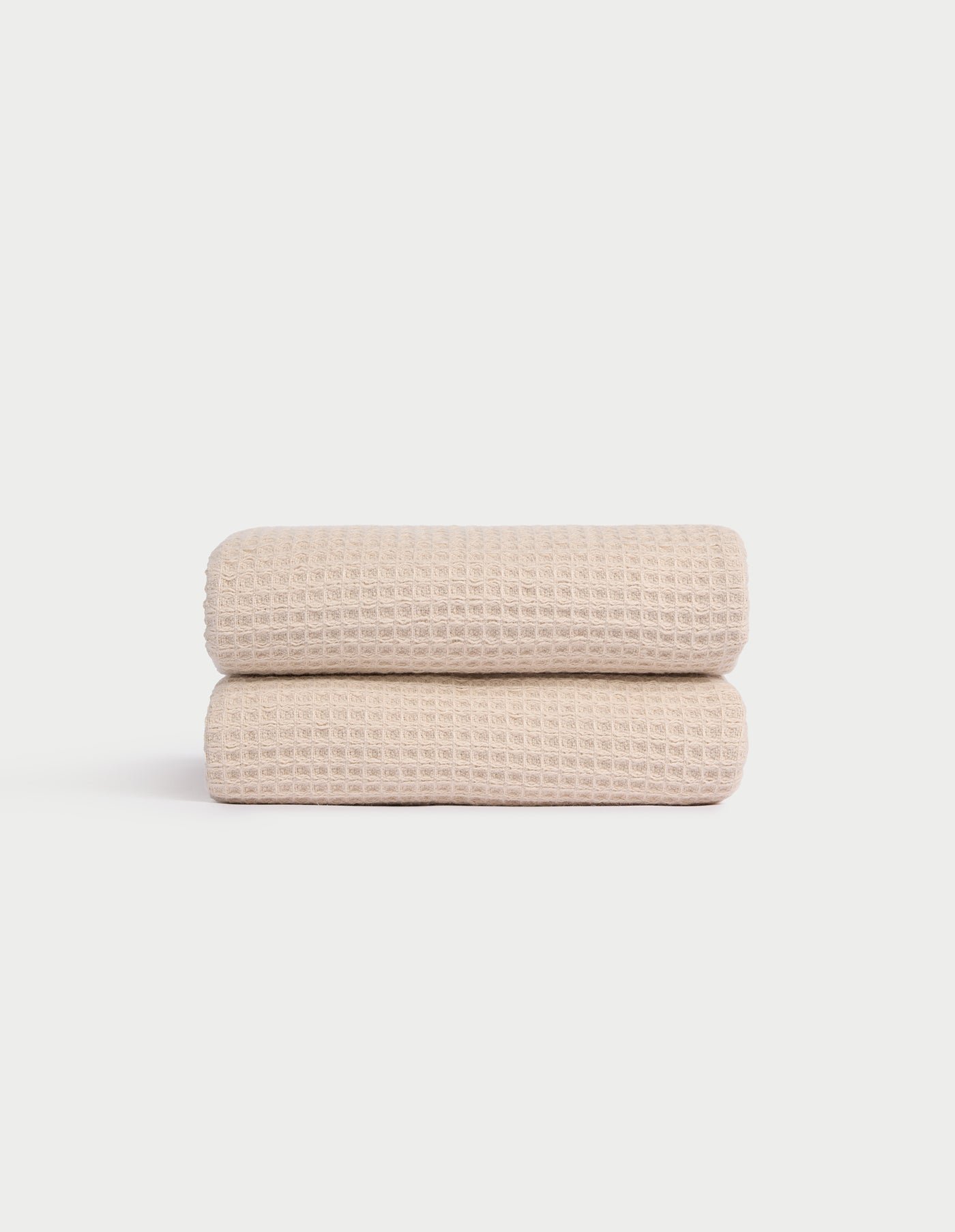 Two Cozy Earth Waffle Hand Towels in light beige are neatly folded and stacked against a plain white background, showcasing their textured pattern. |Color:Birch
