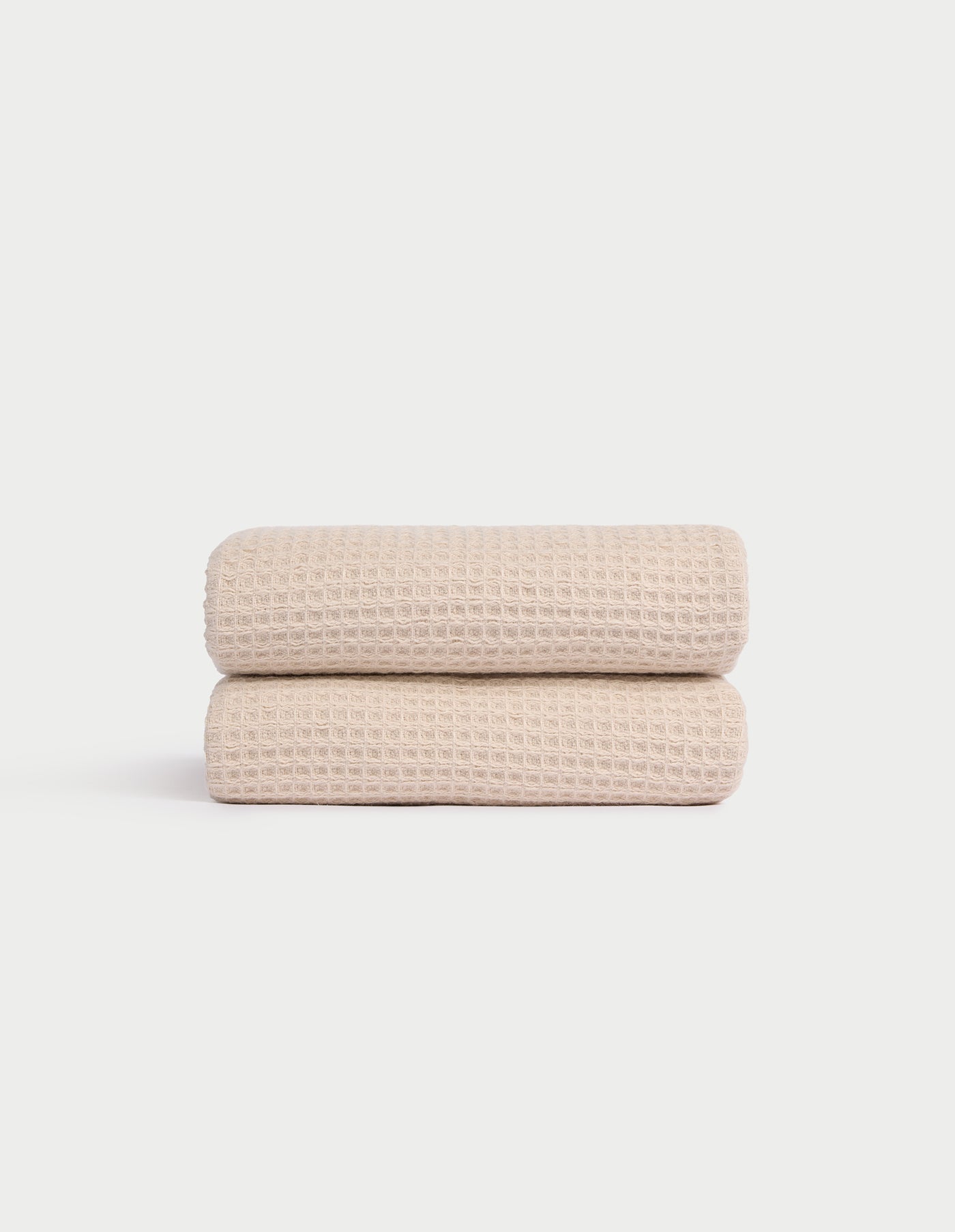 Two Cozy Earth Waffle Hand Towels in light beige are neatly folded and stacked against a plain white background, showcasing their textured pattern. 