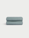 A folded Cozy Earth Waffle Hand Towel in light blue with a textured waffle pattern is displayed on a white background. |Color:Brook