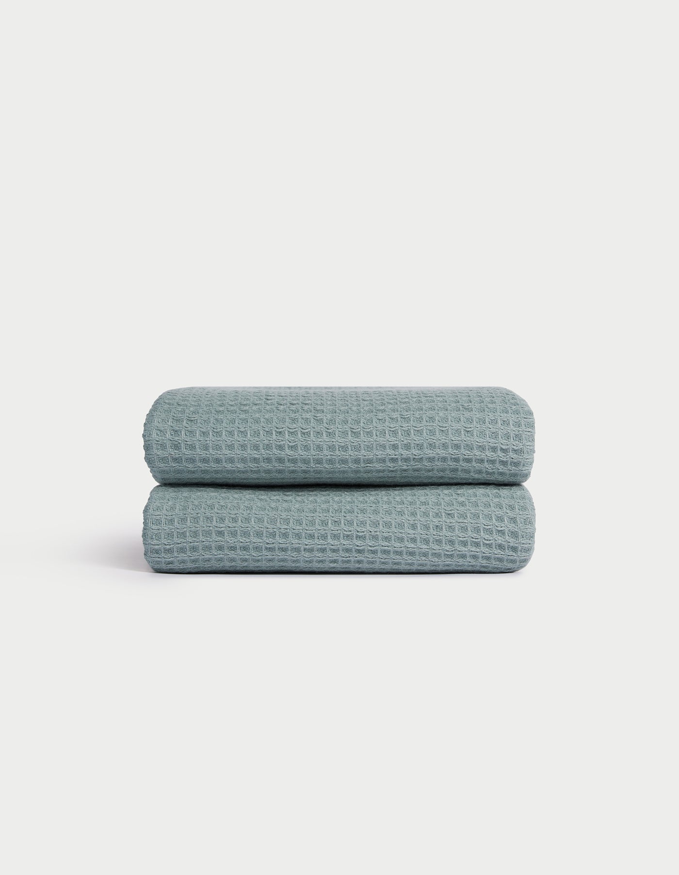 A folded Cozy Earth Waffle Hand Towel in light blue with a textured waffle pattern is displayed on a white background. 