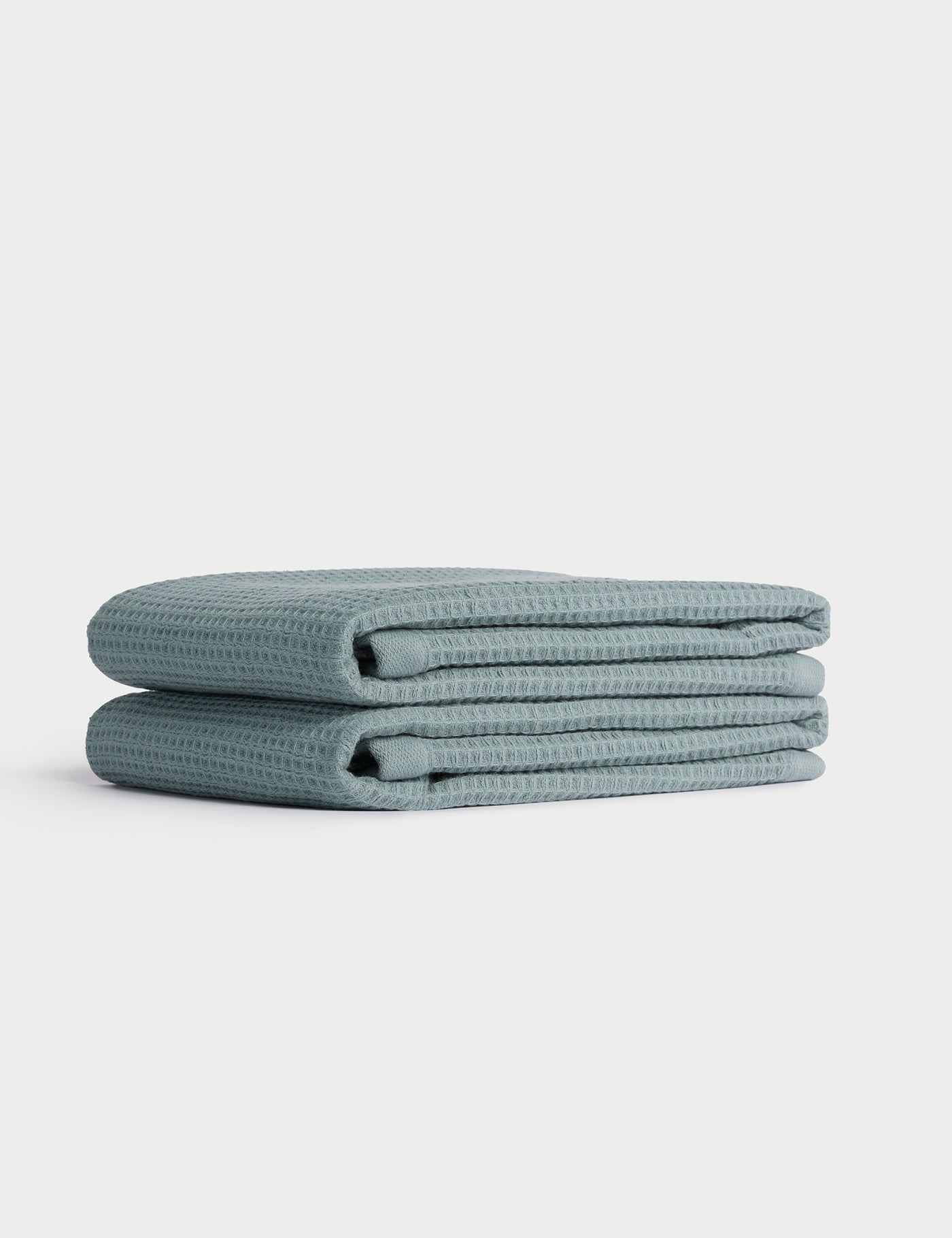 A neatly folded stack of two light blue Cozy Earth Waffle Hand Towels is displayed on a white background. 