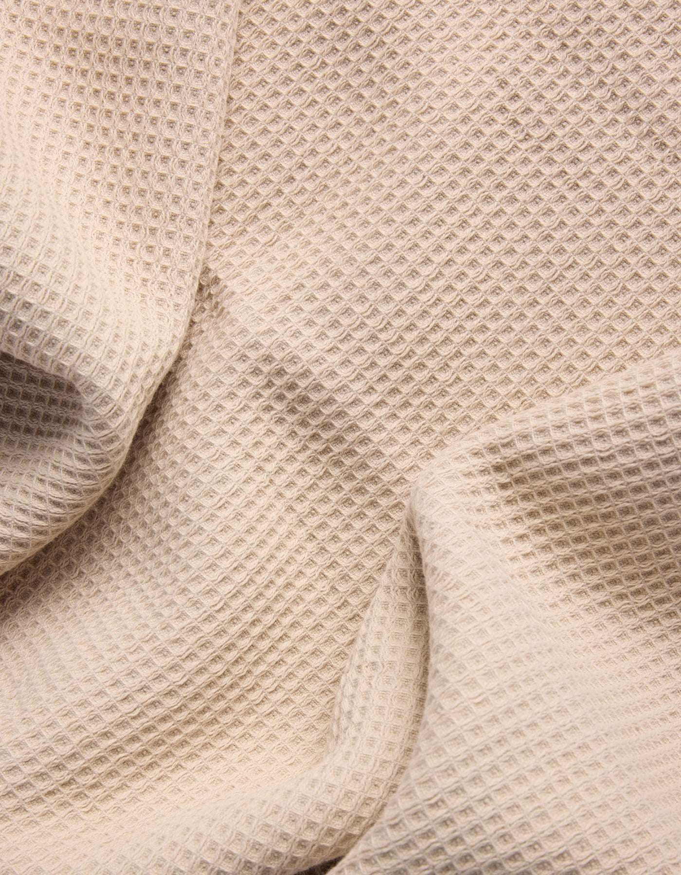 A close-up of Cozy Earth's Waffle Bath Sheets in beige, showing their textured, waffle-like pattern with gentle folds and shadows. 