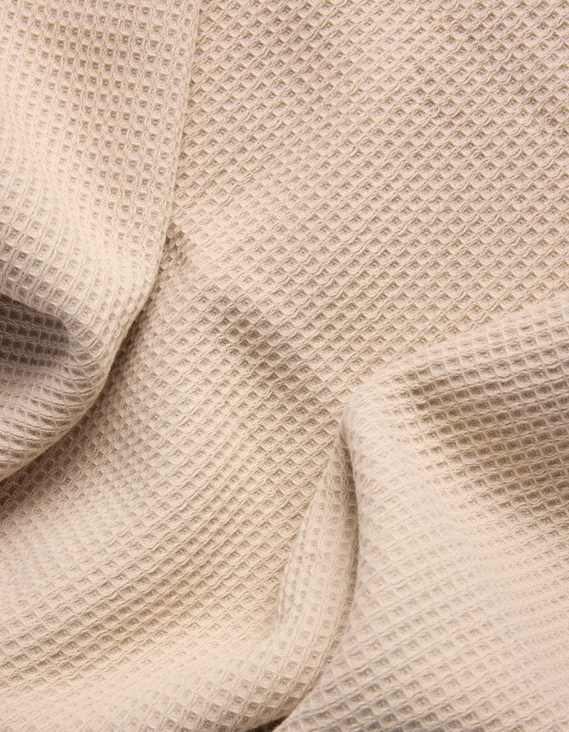 The Cozy Earth Waffle Bath Towel Set features beige waffle-textured fabric with a grid-like pattern, shown draped in soft folds.
