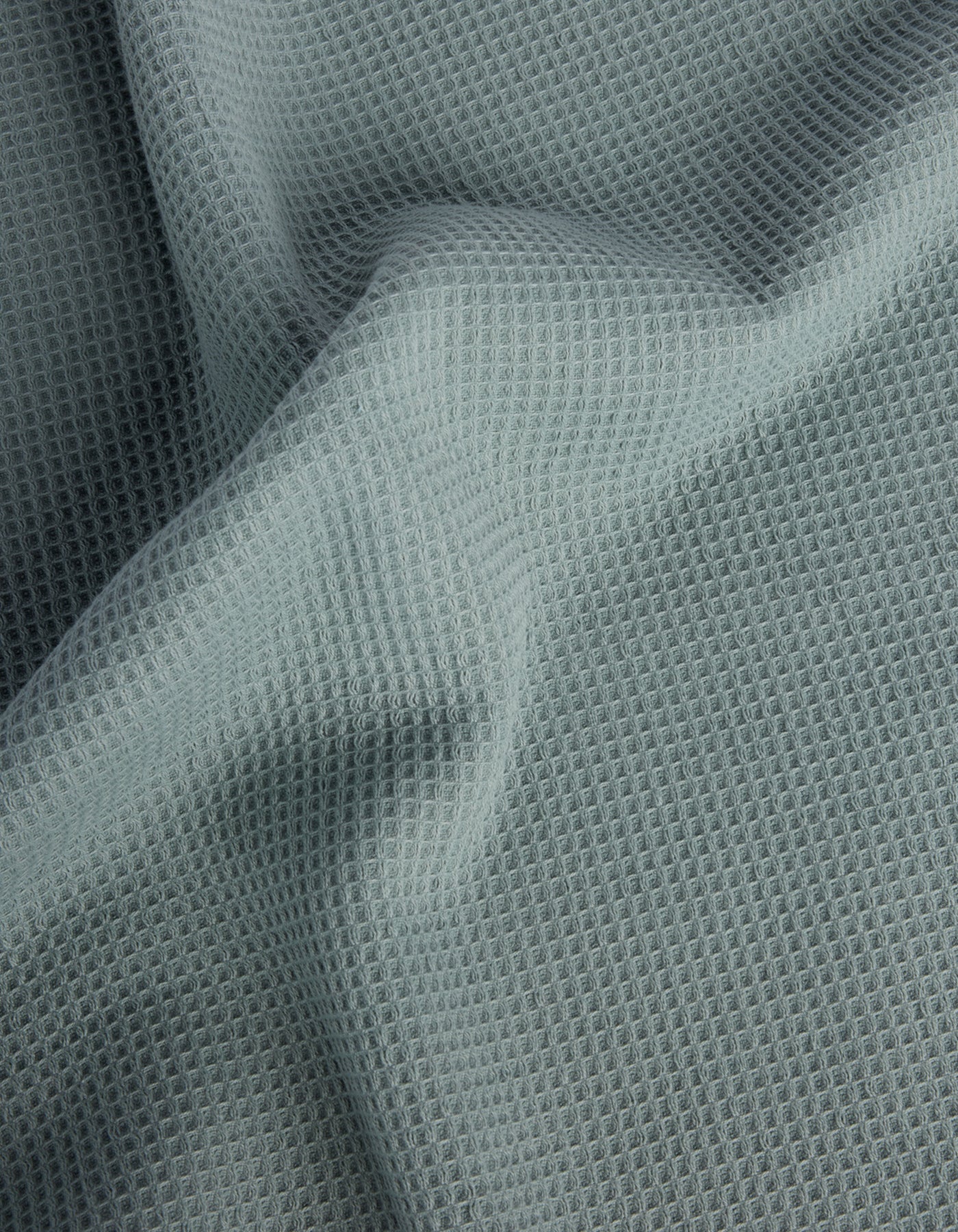 The Cozy Earth Waffle Bath Towel Set features light gray, waffle-textured fabric with a soft, grid-like pattern and gentle folds across the surface. 