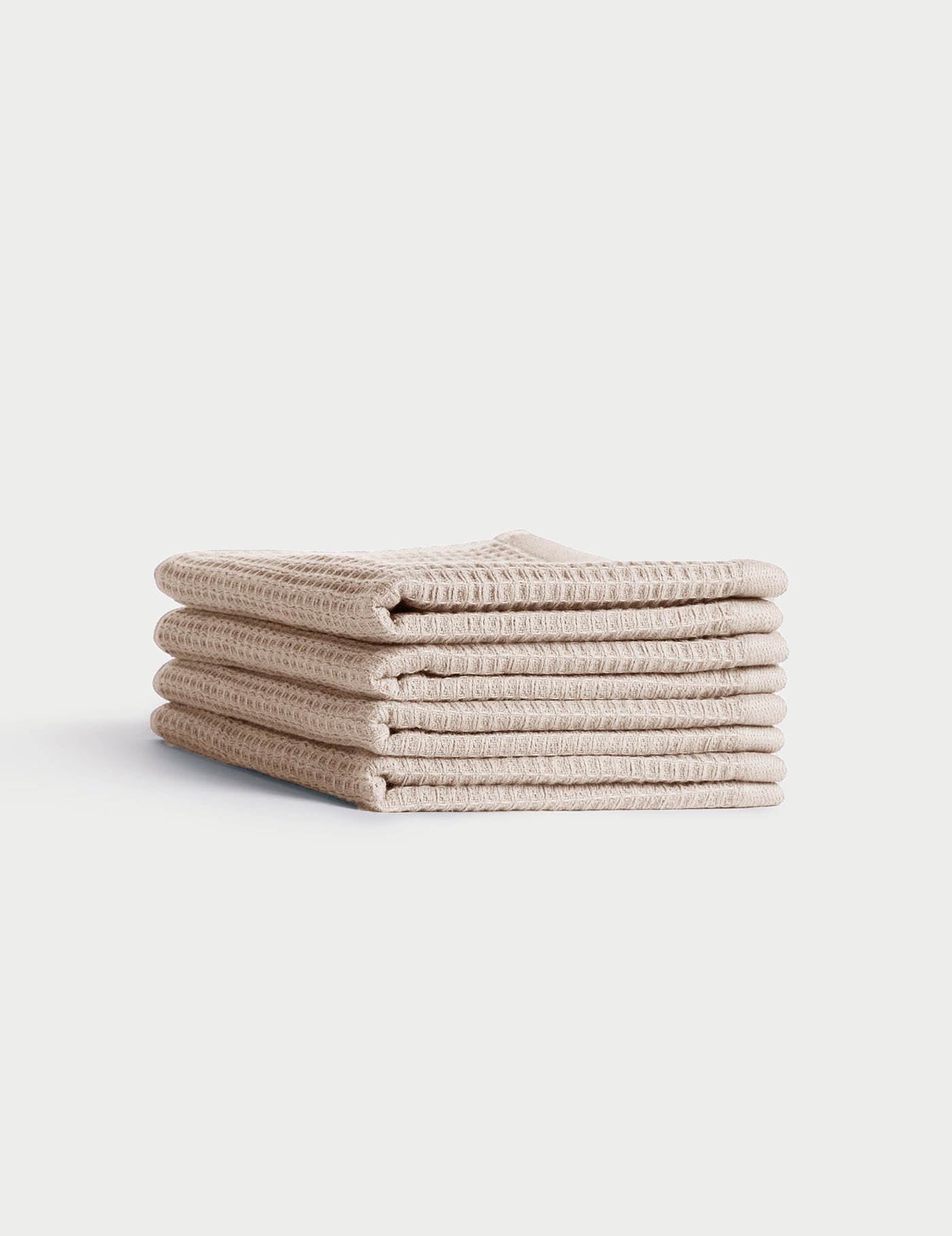 A stack of four neatly folded beige Waffle Washcloths by Cozy Earth, featuring a textured waffle-weave, displayed on a plain white background. 