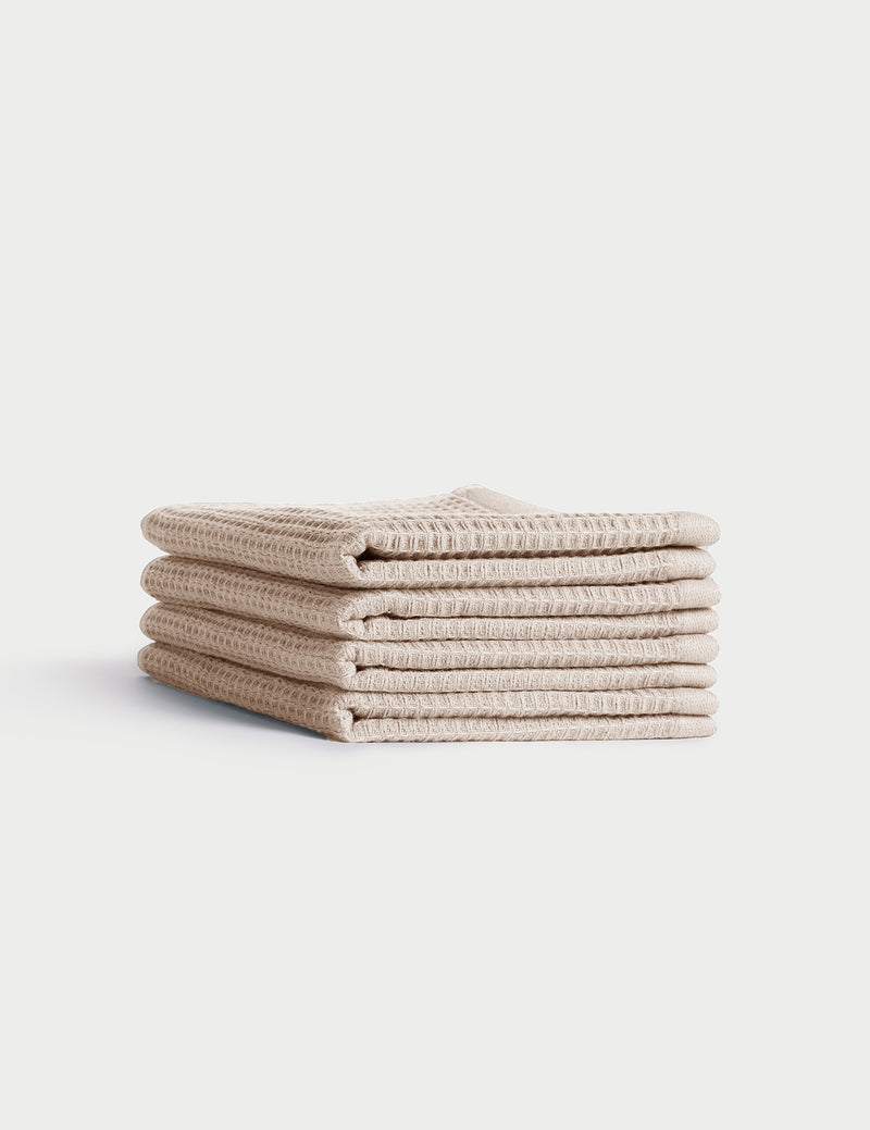A stack of four neatly folded beige Waffle Washcloths by Cozy Earth, featuring a textured waffle-weave, displayed on a plain white background.