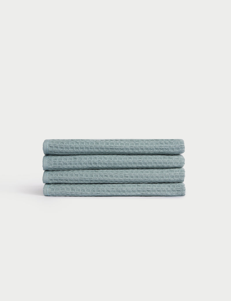 A neatly stacked set of four light blue Cozy Earth Waffle Washcloths with a textured finish on a plain white background.